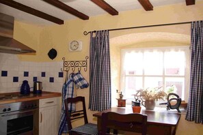 Une cuisine équipée d’une cuisinière, d’un four et d’une horloge au mur. Il y a une fenêtre avec des rideaux et une plante sur le rebord de la fenêtre.