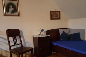 Ein Schlafzimmer mit einem Bett, einem Sessel, einem Schreibtisch mit Lampe und zwei gerahmten Bildern an der Wand.