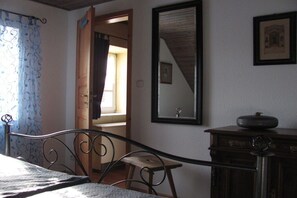 Ein Schlafzimmer mit einem Bett, einem Holzstuhl, einer Kommode, einem Spiegel und einer Tür zu einem anderen Raum.