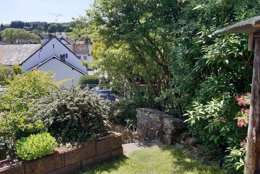 A residential garden with a stone wall, various shrubs, and a view of houses in the background.