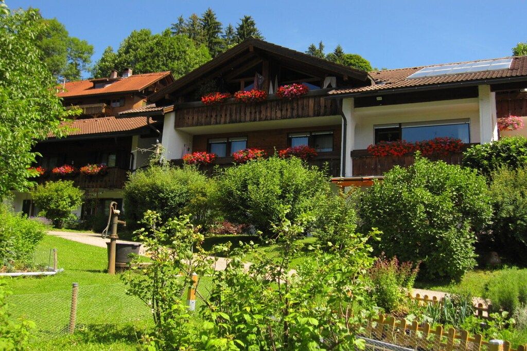 A multi-story building with balconies, surrounded by lush greenery and a clear sky.