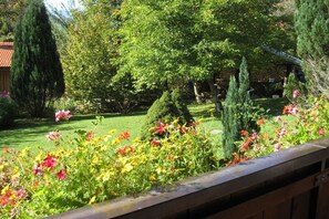 Ein Garten mit verschiedenen Pflanzen und Blumen, einer gepflegten Rasenfläche und einer Steinmauer im Hintergrund.
