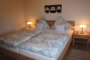 Ein Doppelbett mit gemustertem Überwurf, zwei Nachttische mit Lampen und ein an der Wand hängendes Blumenbild.