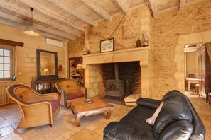 Ein gemütliches Wohnzimmer mit Kamin aus Stein, Holzbalken, Korbmöbeln und einer Ledersofa.