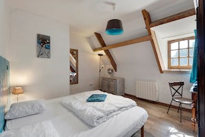 Ein Schlafzimmer mit einem Bett, einem Heizkörper, einem Ventilator, einem Fenster und einem Gemälde an der Wand.