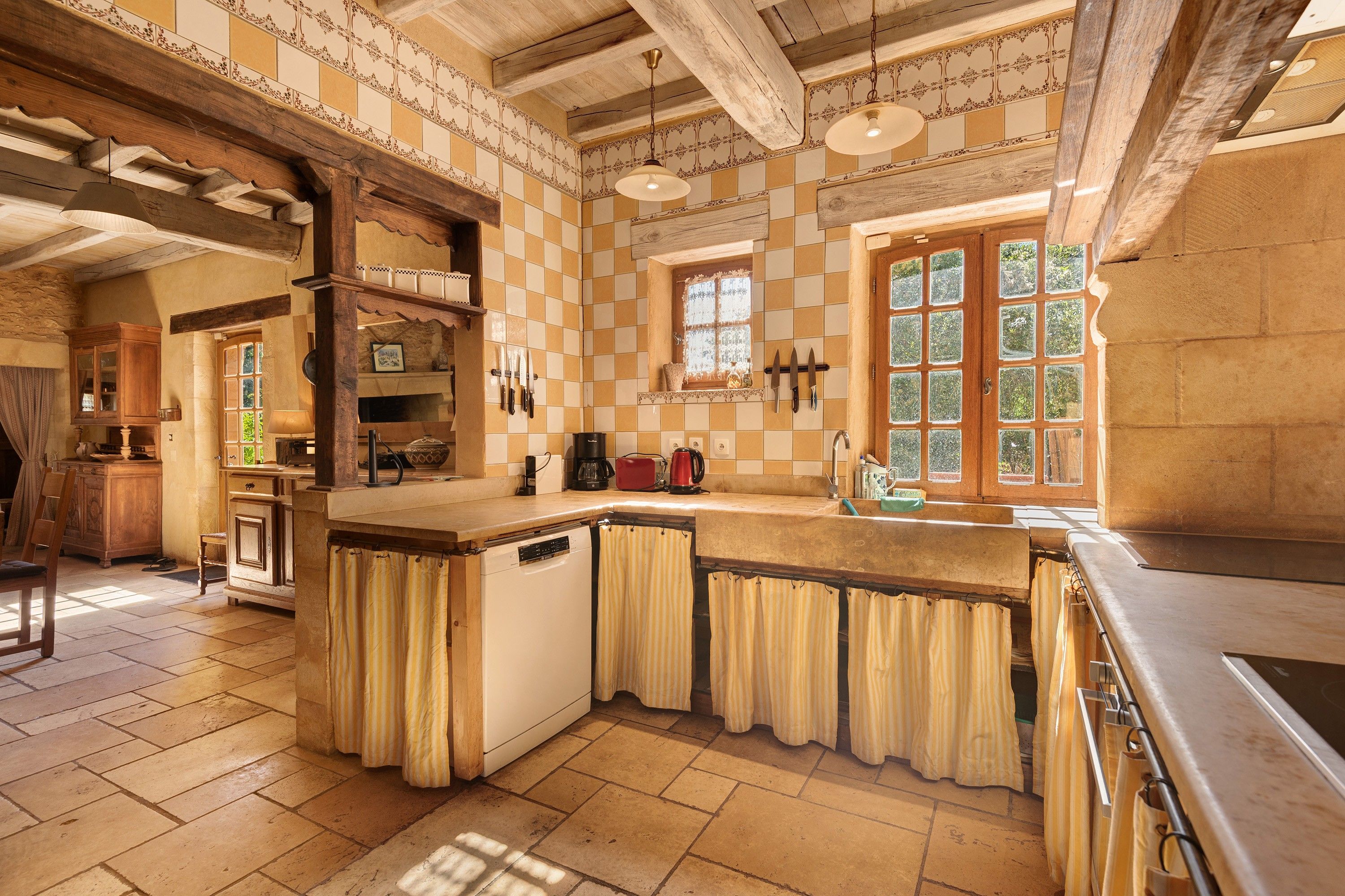 A kitchen with a checkered tile backsplash, wooden beams, and a large window with a view of greenery.