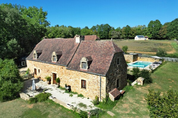 Una casa in pietra con tetto spiovente, piscina e cortile recintato.