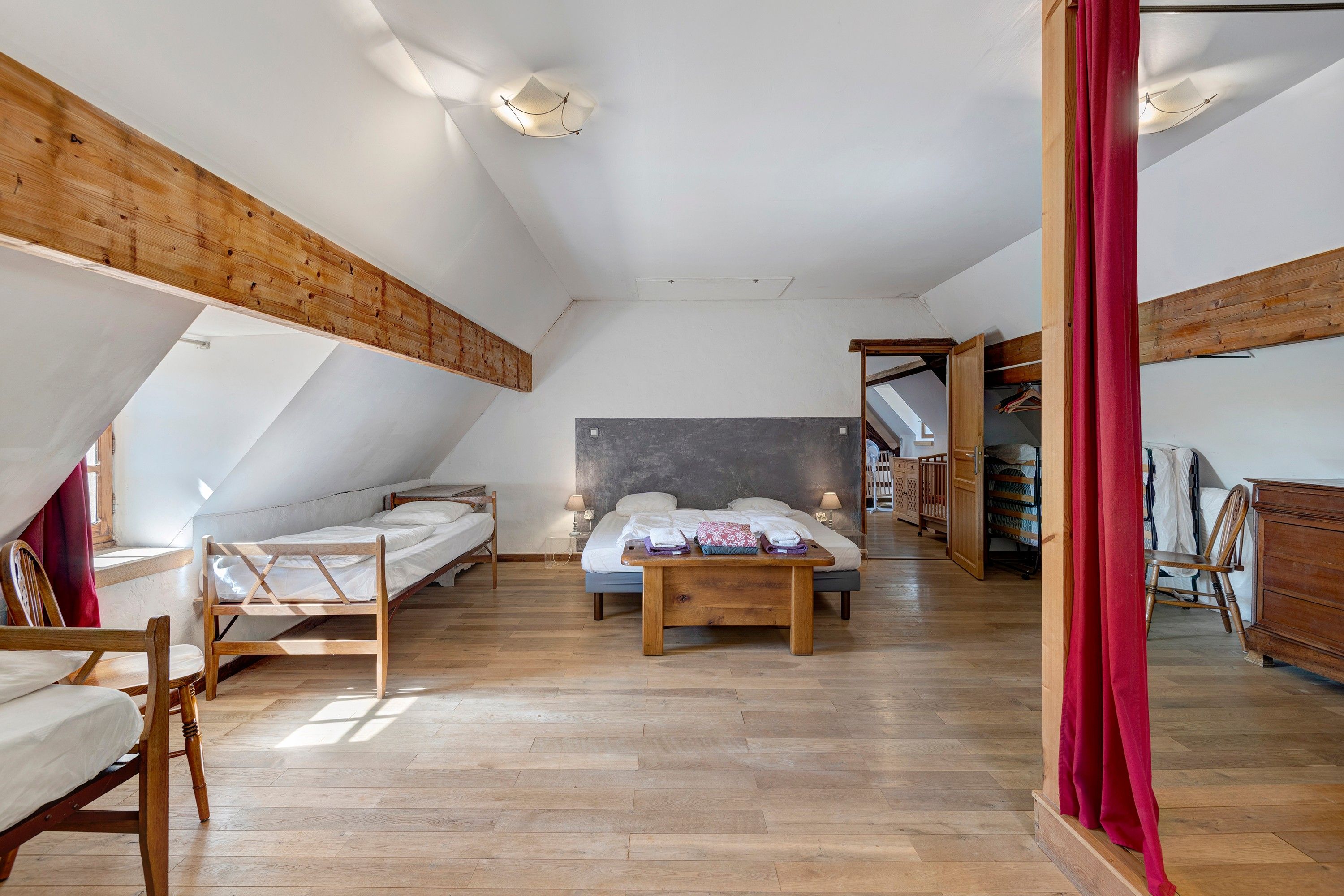 Una habitación con techo inclinado, vigas de madera, una cama con cabecera, un banco y un armario.