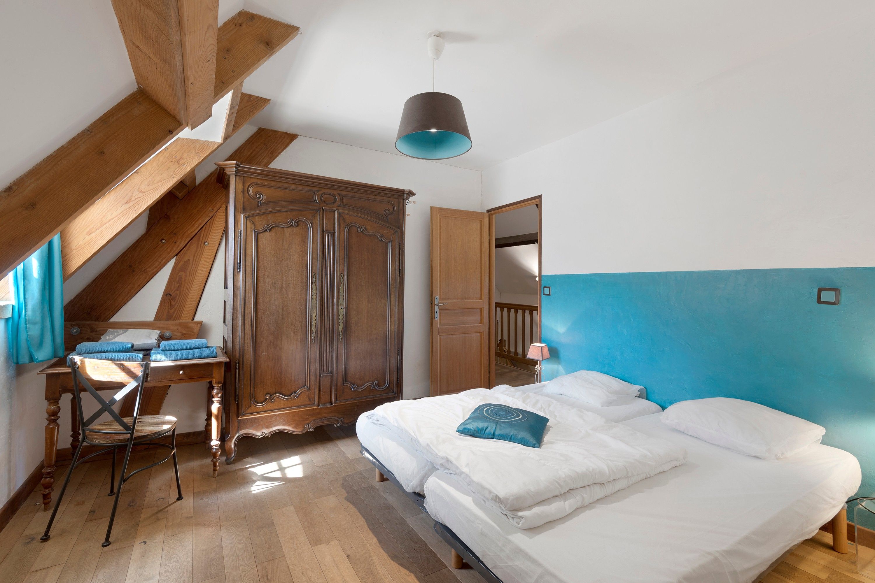 Ein Schlafzimmer mit einem Holzschrank, einem Bett mit weißer Bettwäsche, einem Schreibtisch mit Stuhl und einer blauen Wand.
