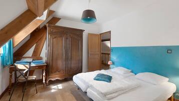 Ein Schlafzimmer mit einem Holzschrank, einem Bett mit weißer Bettwäsche, einem Schreibtisch mit Stuhl und einer blauen Wand.