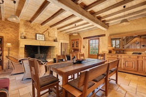 A rustic interior with a stone fireplace, wooden dining table, and a kitchen area.