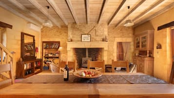 Ein rustikaler Essraum mit Holztisch, Stühlen, Kamin und einer Steinwand.