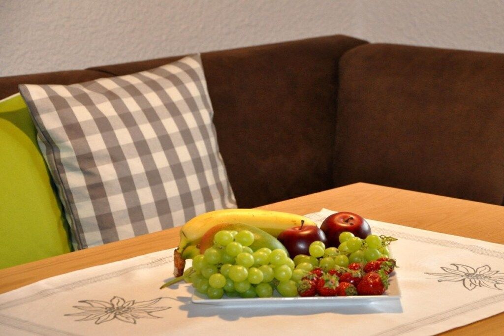 A fruit platter on a table with a checkered pillow and a brown couch in the background.