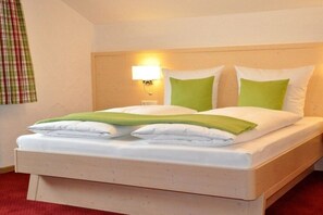 A single bed with white bedding and green pillows, a bedside lamp, and a window with a plaid curtain. - 2 in the country house Magdalena (Oberstdorf)