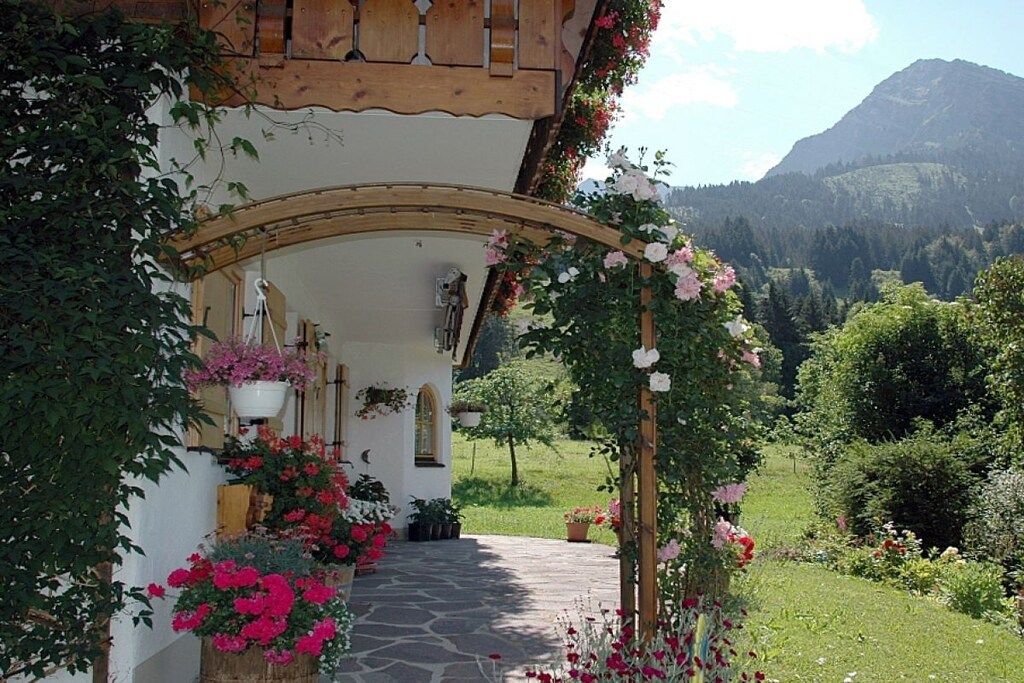 A rustic building with a stone pathway leading to an archway adorned with flowers.