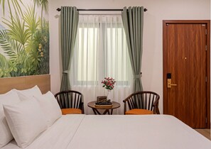 Ett hotellrum med en säng, två stolar, ett litet bord med en vas och en dörr.
