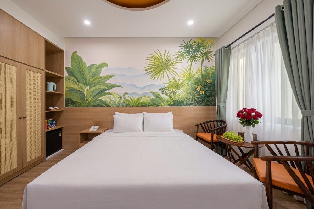 Quarto de hotel com cama, escrivaninha, cadeira, guarda-roupa e um mural de paisagem tropical.