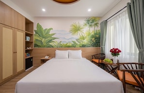 Una habitación de hotel con cama, escritorio, silla, armario y un mural de paisaje tropical.