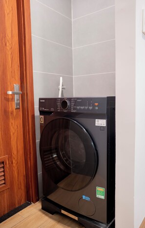 Eine kompakte, moderne Waschmaschine in einem kleinen Waschraum mit Holztür und gefliesten Wänden.