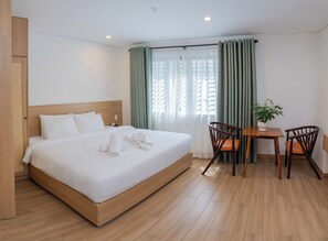 Ein Hotelzimmer mit einem großen Bett, einem hölzernen Kopfteil, einem kleinen Tisch mit Stühlen und einer Zimmerpflanze.
