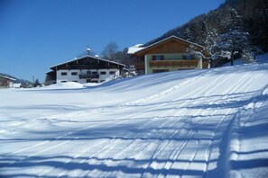 Une piste de ski enneigée avec deux bâtiments : l’un doté d’un balcon et l’autre d’un toit en pente.