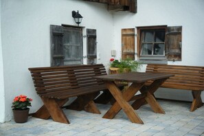 A patio with wooden benches and a table, a potted plant, and a wall-mounted lamp. - Spitzstein on the Bergerhof (Aschau im Ch. \/Sachrang)