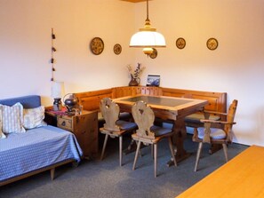 Une pièce confortable avec un lit, une table à manger en bois avec des chaises, une petite table d’appoint et une lampe fixée au mur.