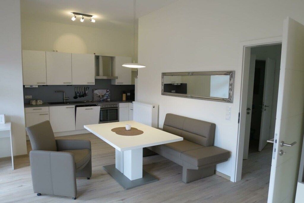 Een moderne keuken met witte kasten, een eettafel met stoelen en een inbouwoven.