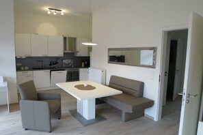 A modern kitchen with white cabinets, a dining table with chairs, and a built-in oven. - Villa Ariana FW Viola (Borkum)