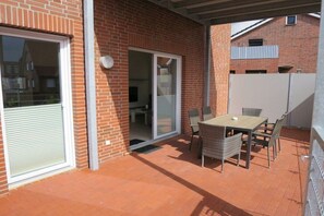 A patio with a table and chairs, a sliding glass door, and a brick wall. - Villa Ariana FW Viola (Borkum)
