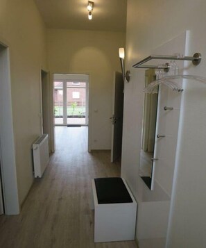 Een smalle gang met een witte bank, een deur met een handdoekhouder en een radiator aan de muur.