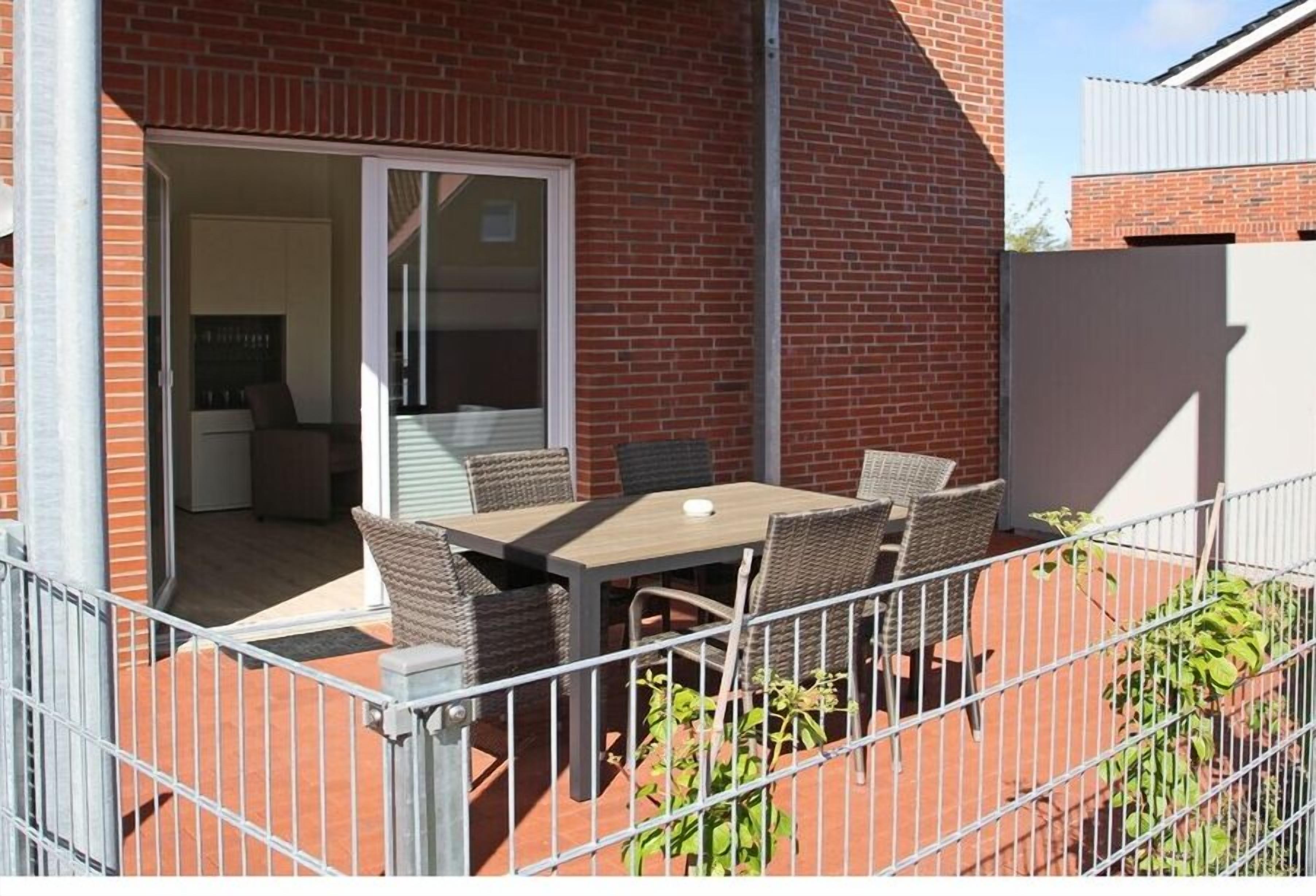 Un patio con una mesa, sillas, un ventanal corredero y un muro de ladrillo.