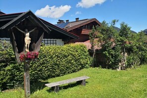 Eine Holzkonstruktion mit einer Statue, einer Bank und einem Haus im Hintergrund.