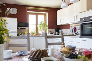 Eine Küche mit weißen Schränken, einer Mikrowelle, einer Uhr und einem Fenster mit einer Pflanze.