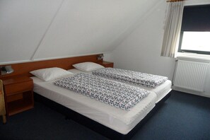 Een kamer met twee bedden, een houten hoofdbord, een nachtkastje, een raam met gordijnen en een radiator.