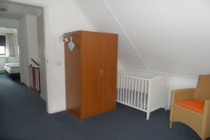 A room with a wooden wardrobe, a white crib, and a wicker chair. - Holiday home with 1 bedroom (Julianadorp aan Zee)