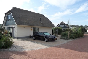 A single-story building with a sloped roof, a car parked in front, and a gravel driveway. - Holiday home with 1 bedroom (Julianadorp aan Zee)