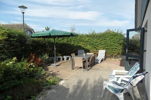 Een terras buiten met een tafel, stoelen, een groene parasol en een witte stoel.