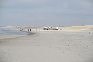 A beach with a building on stilts, a sandy shore, and a few people walking. - Holiday home with 1 bedroom (Julianadorp aan Zee)