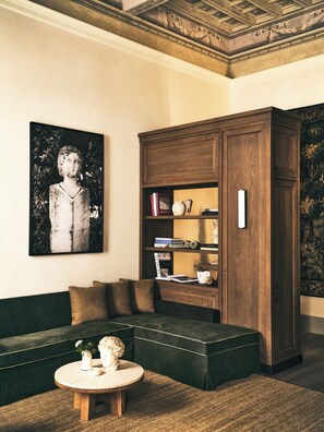 A room with a dark green sofa, a round wooden coffee table, and a large wooden cabinet with shelves. - La Réserve Firenze (Firenze)