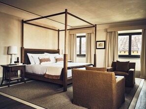 A four-poster bed with a wooden frame, a bedside table with a lamp, a chair, and a window with curtains. - La Réserve Firenze (Firenze)