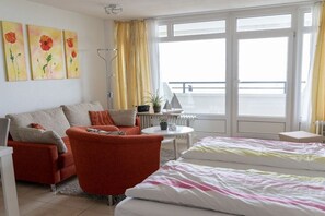 A hotel room with a bed, a sofa, a chair, a small table, and a window with curtains. - Luca Panorama Apt. 16, 1st floor (Cuxhaven\/Duhnen)