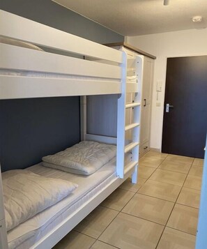 Een stapelbed met een ladder, een deur en een betegelde vloer.