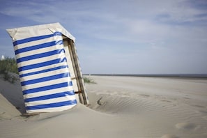 A beach with a striped beach umbrella and a wooden structure. - Holiday apartment Trientje (Borkum)