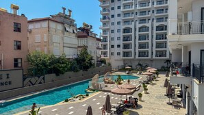 Un espace piscine aménagé sur le toit, avec des chaises longues et des parasols, entouré d’immeubles dotés de balcons.