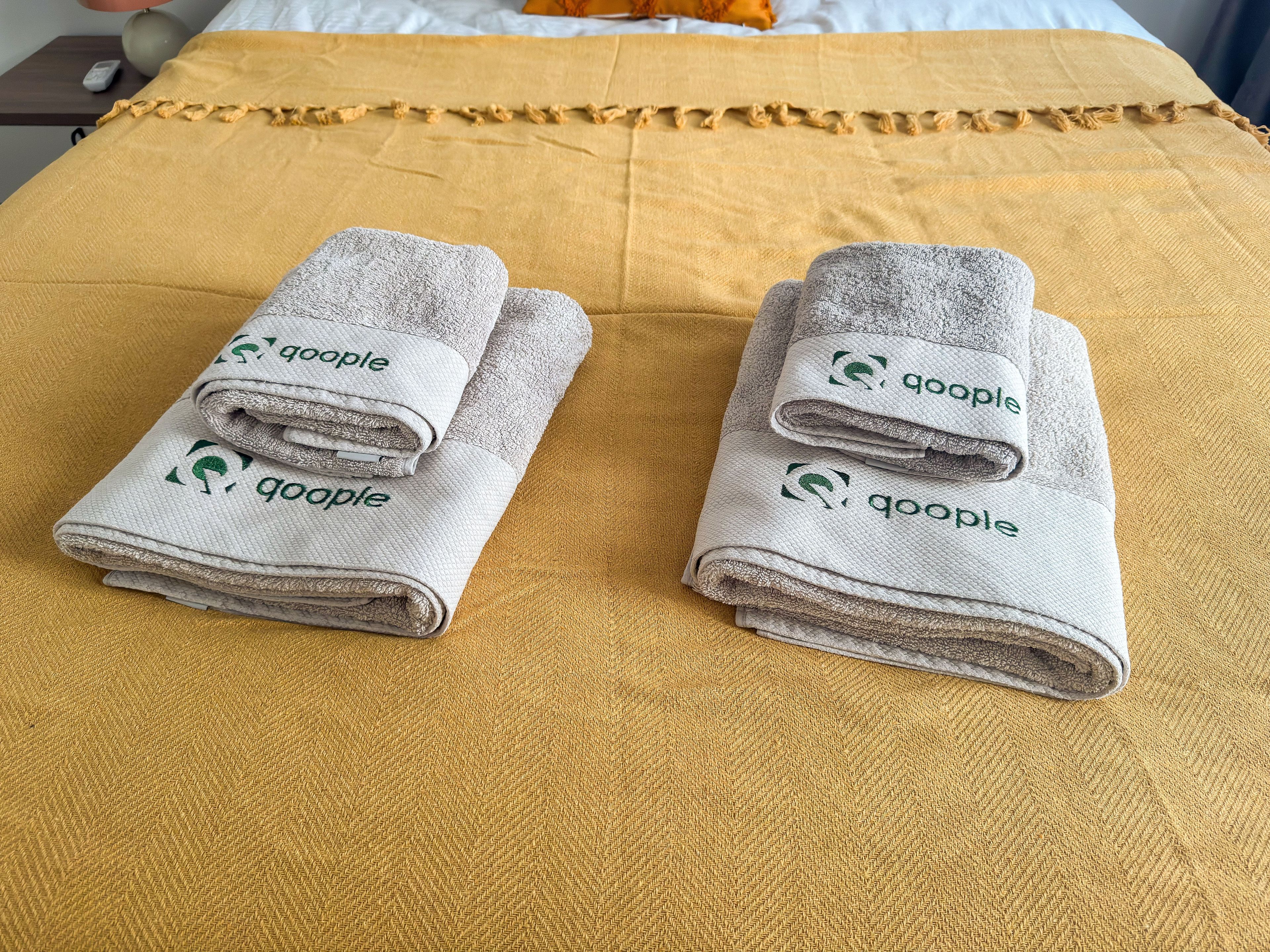 Two folded towels with 'Google' branding on a bed with a yellow bedspread.