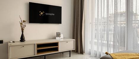 Una sala de estar moderna con un televisor de pantalla plana montado en la pared, una consola blanca y un gran ventanal con cortinas translúcidas.