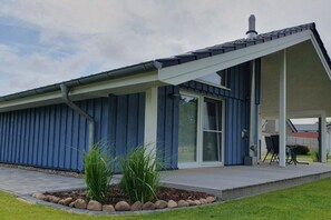 A modern building with a covered patio area, a large window, and a chimney. - Holiday home with 1 bedroom (Wurster Nordseeküste)