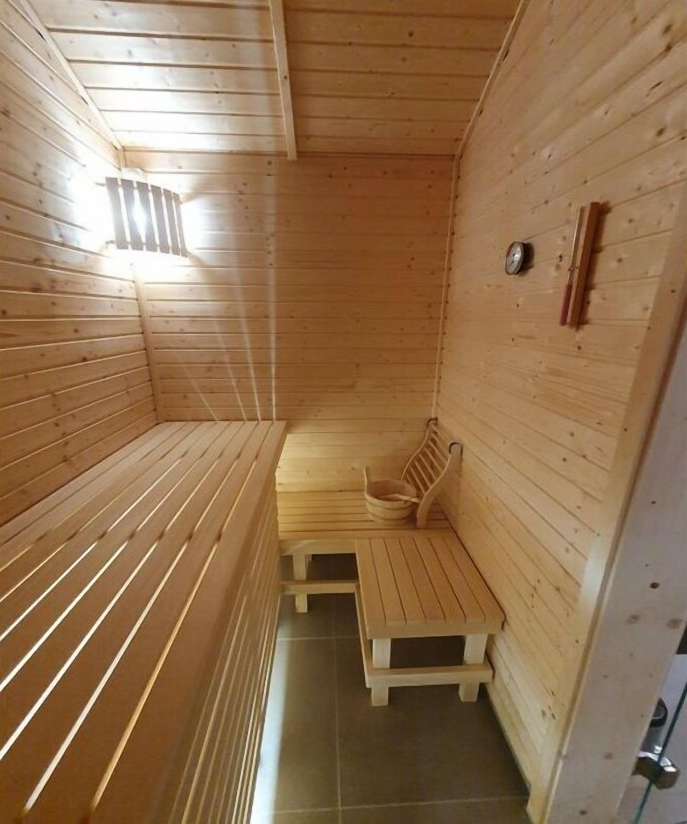 Una sauna con bancos de madera, un asiento y un calentador fijado a la pared.
