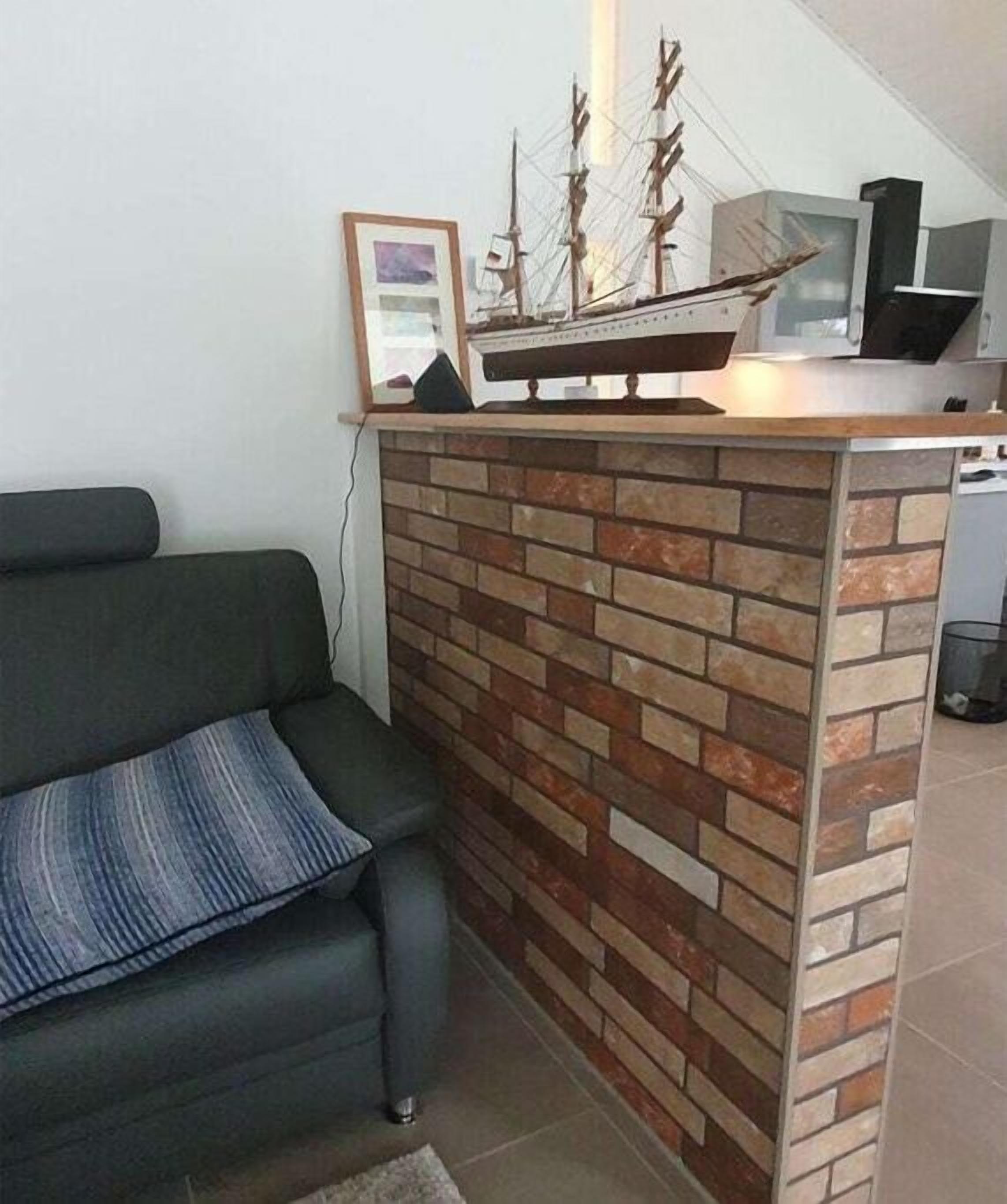 A living area with a sofa, a brick accent wall, a ship model, and a television.